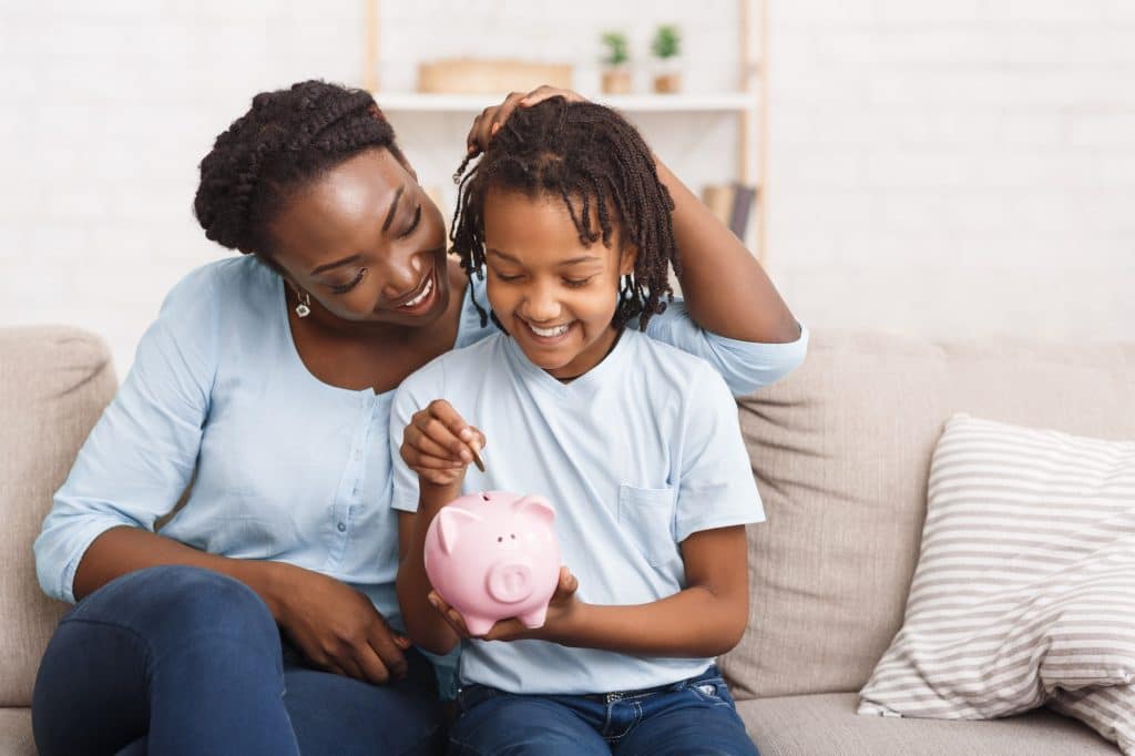 Little black girl putting money to piggy bank