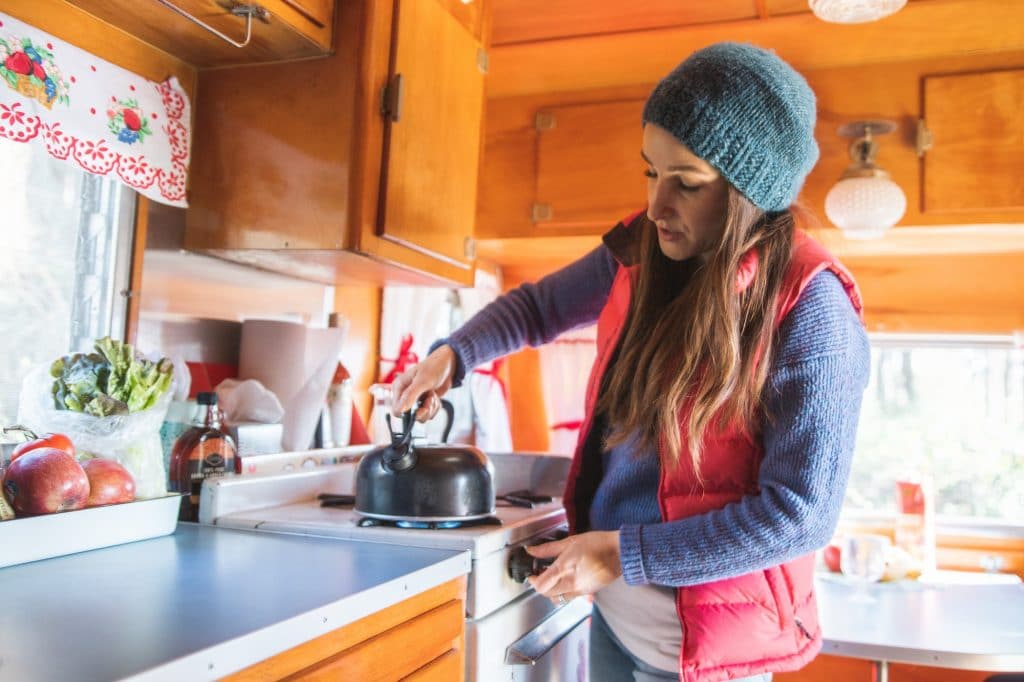 woman in vintage RV camping trailer boiling a kettle on the stove