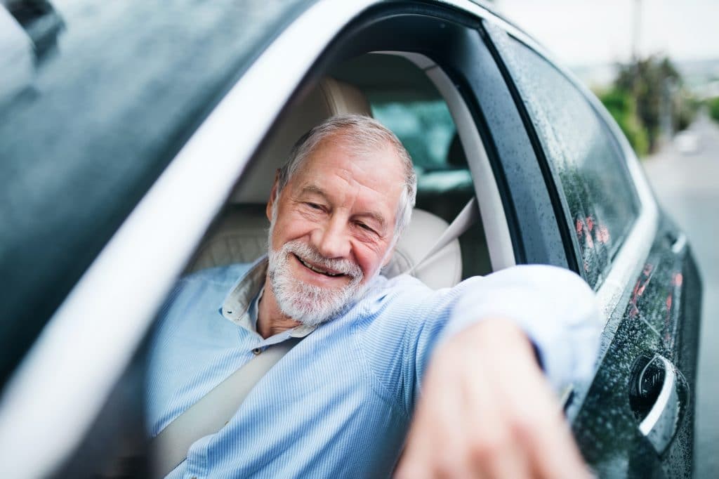 Happy senior man sitting in car in driver seat