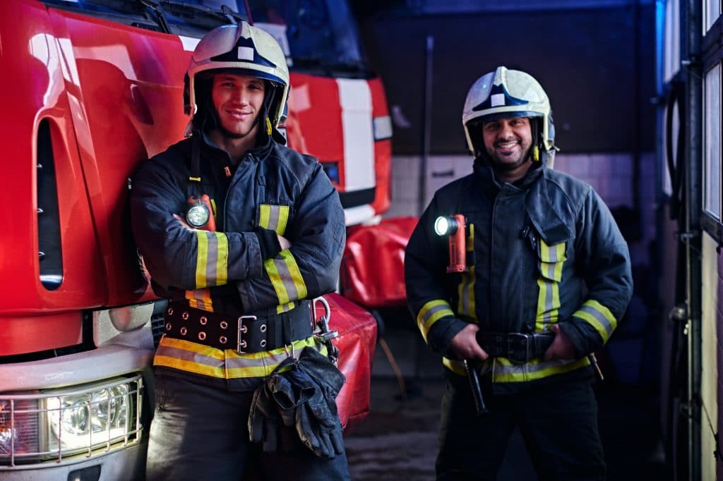 Two firemen standing near the fire truck at night in a fire depot