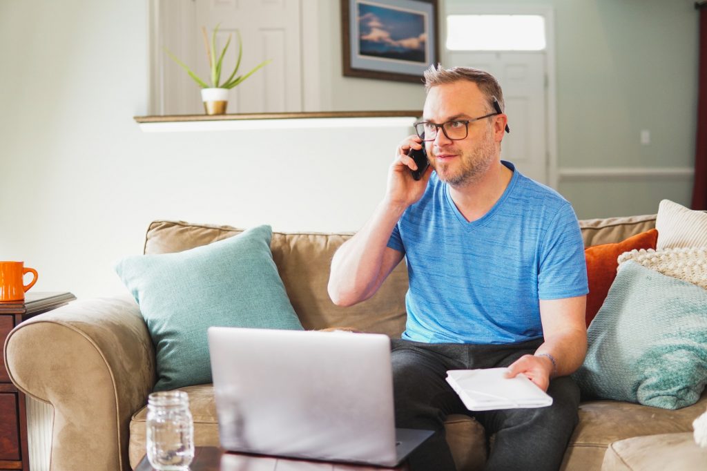 Man working from home on laptop computer talking on phone conference call or paying bills and doing