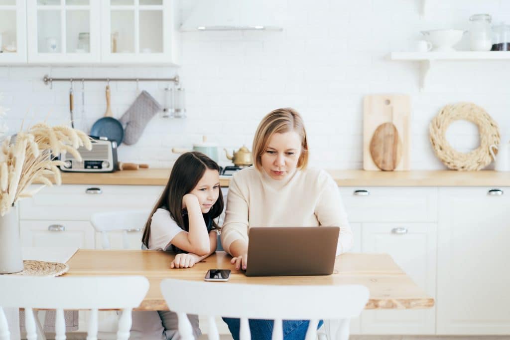 Mom and daughter at the table in the kitchen with a laptop work, study and communicate online.