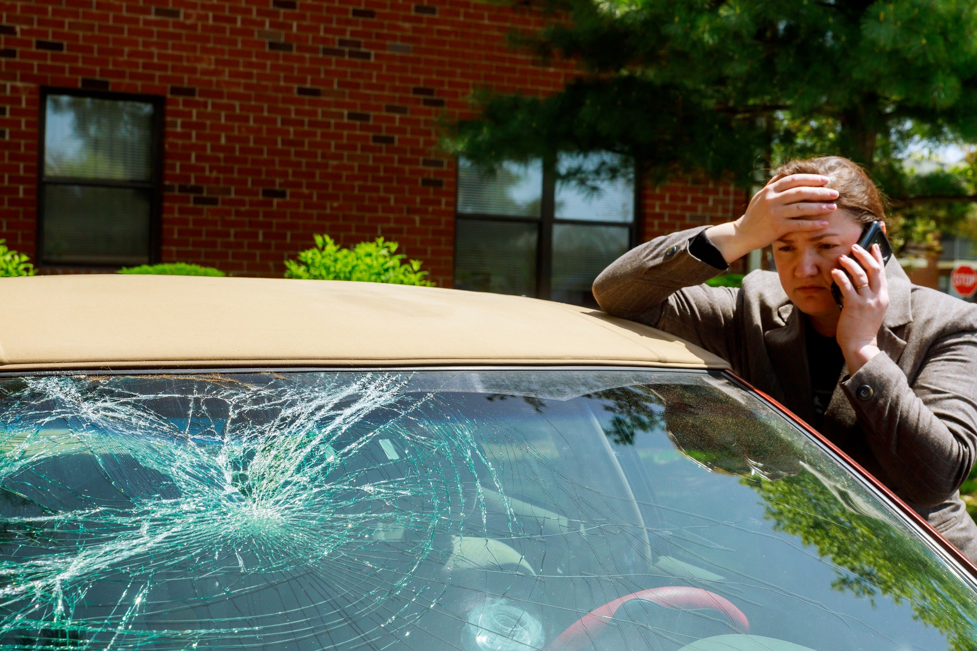 Woman making a phone call next to broken windshield after a car accident