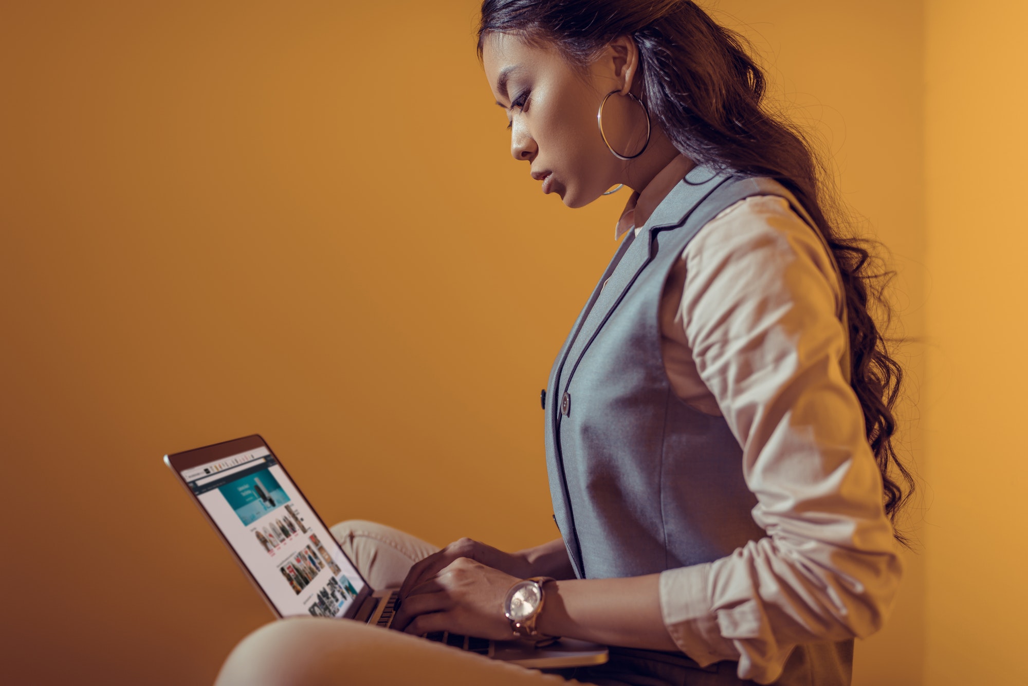 asian businesswoman using laptop with amazon website in front of orange wall