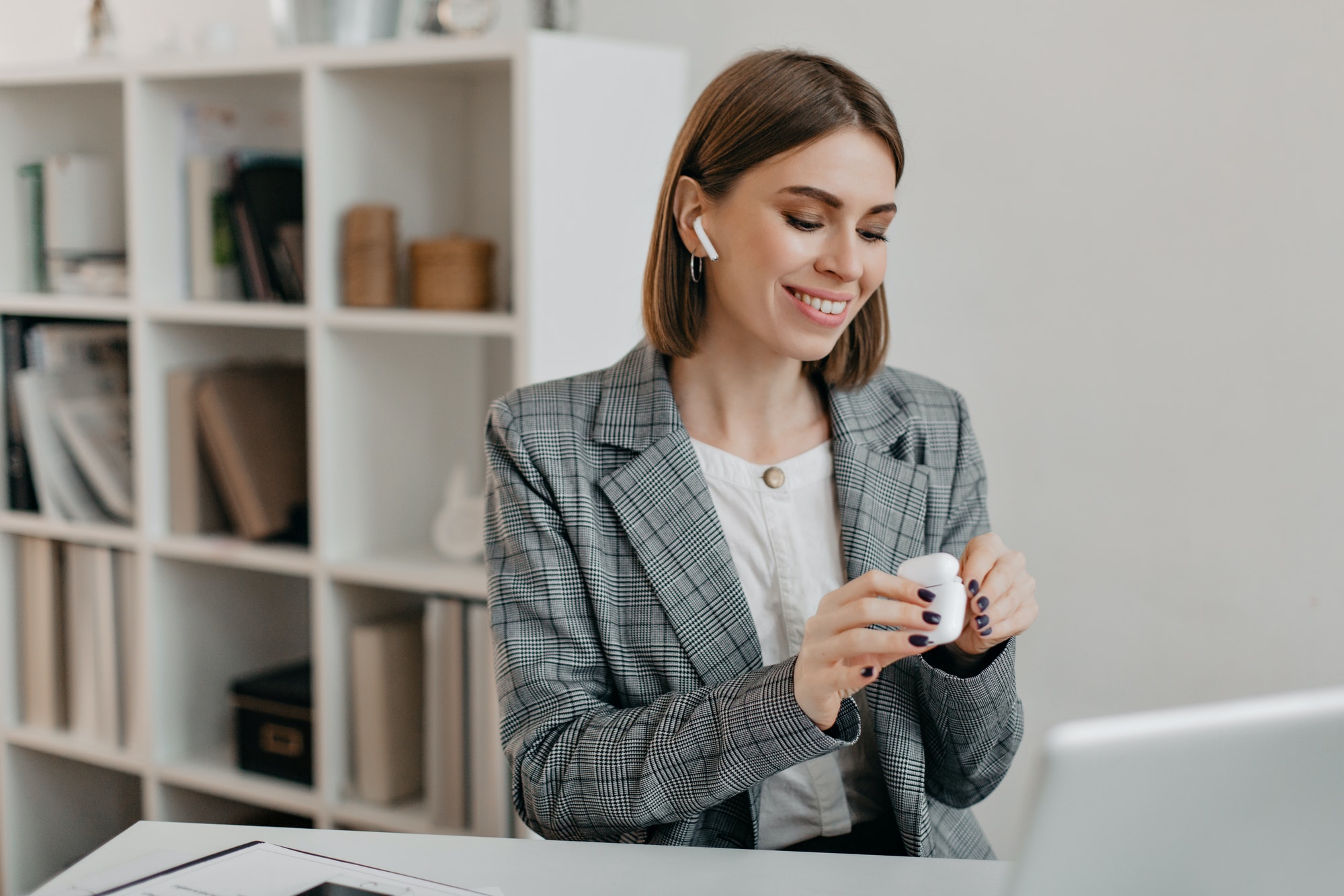 Portrait of smiling woman in office outfit putting on airpods to communicate with customers