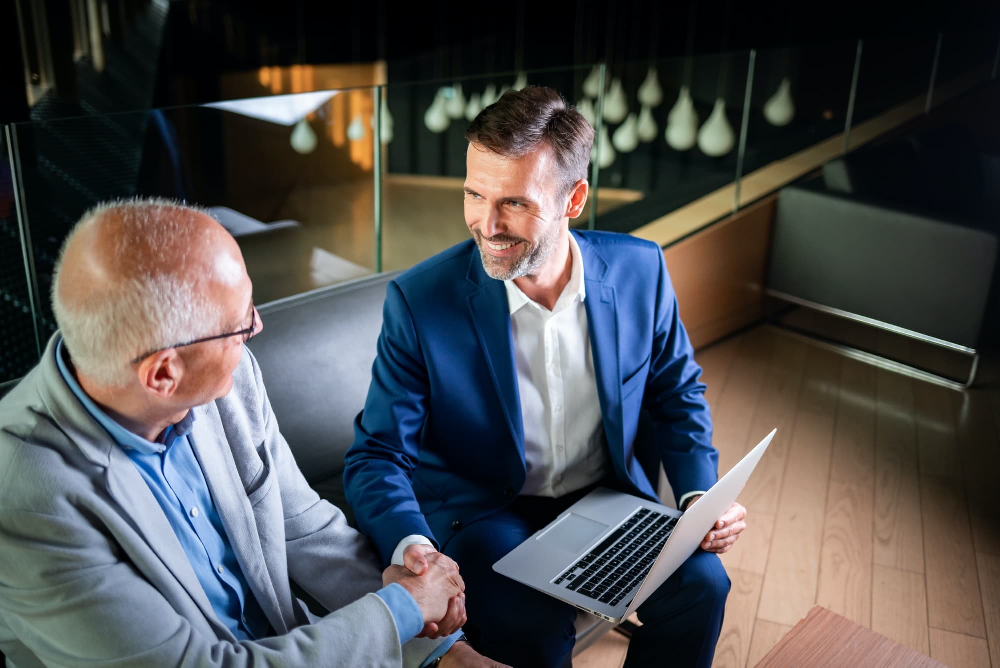 Younger and older businessman shaking hands in modern business lounge