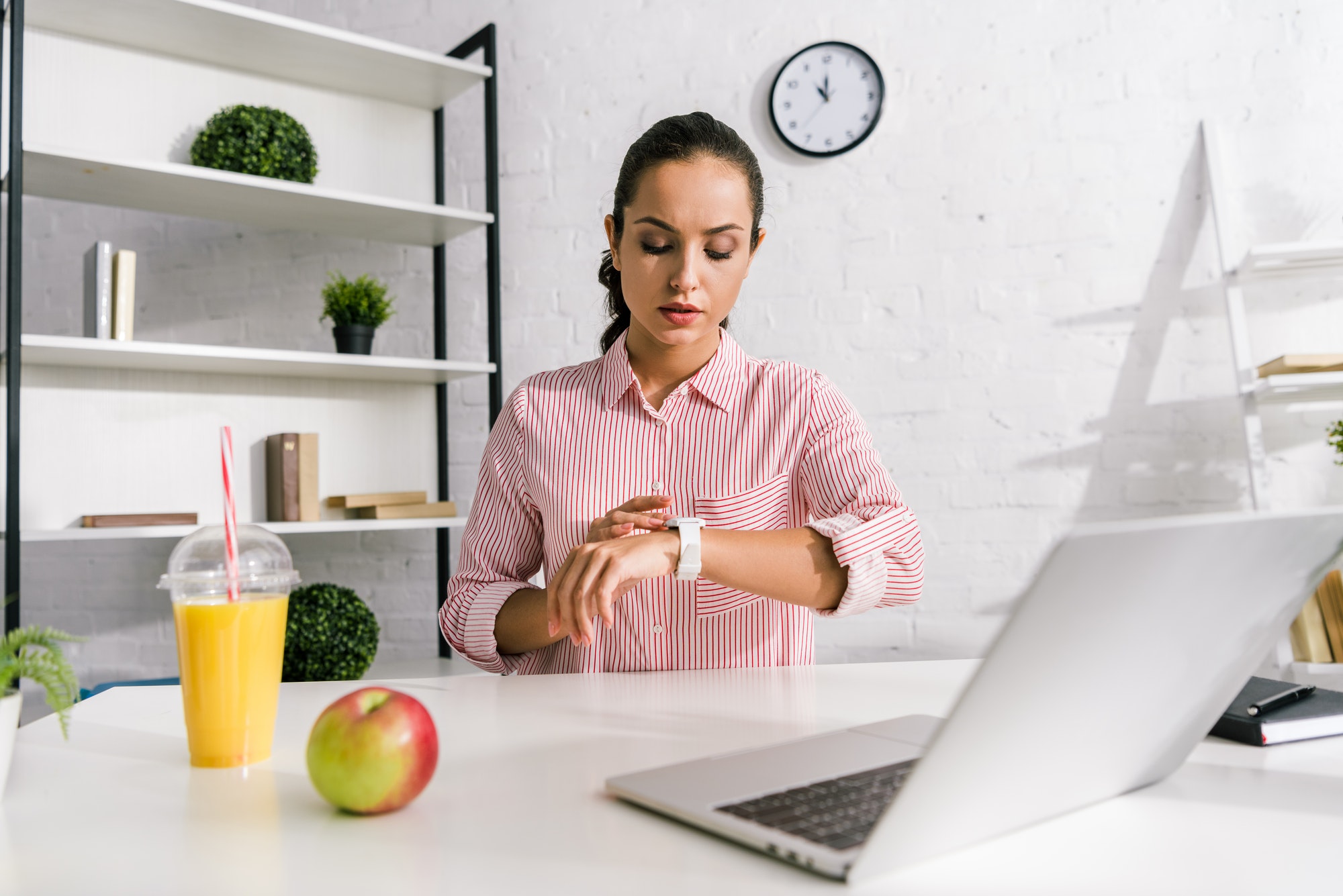 attractive girl looking at watch near laptop and apple