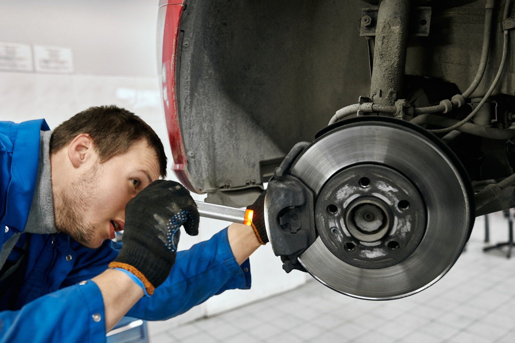 Male mechanic holding flashlight and examining brake pads