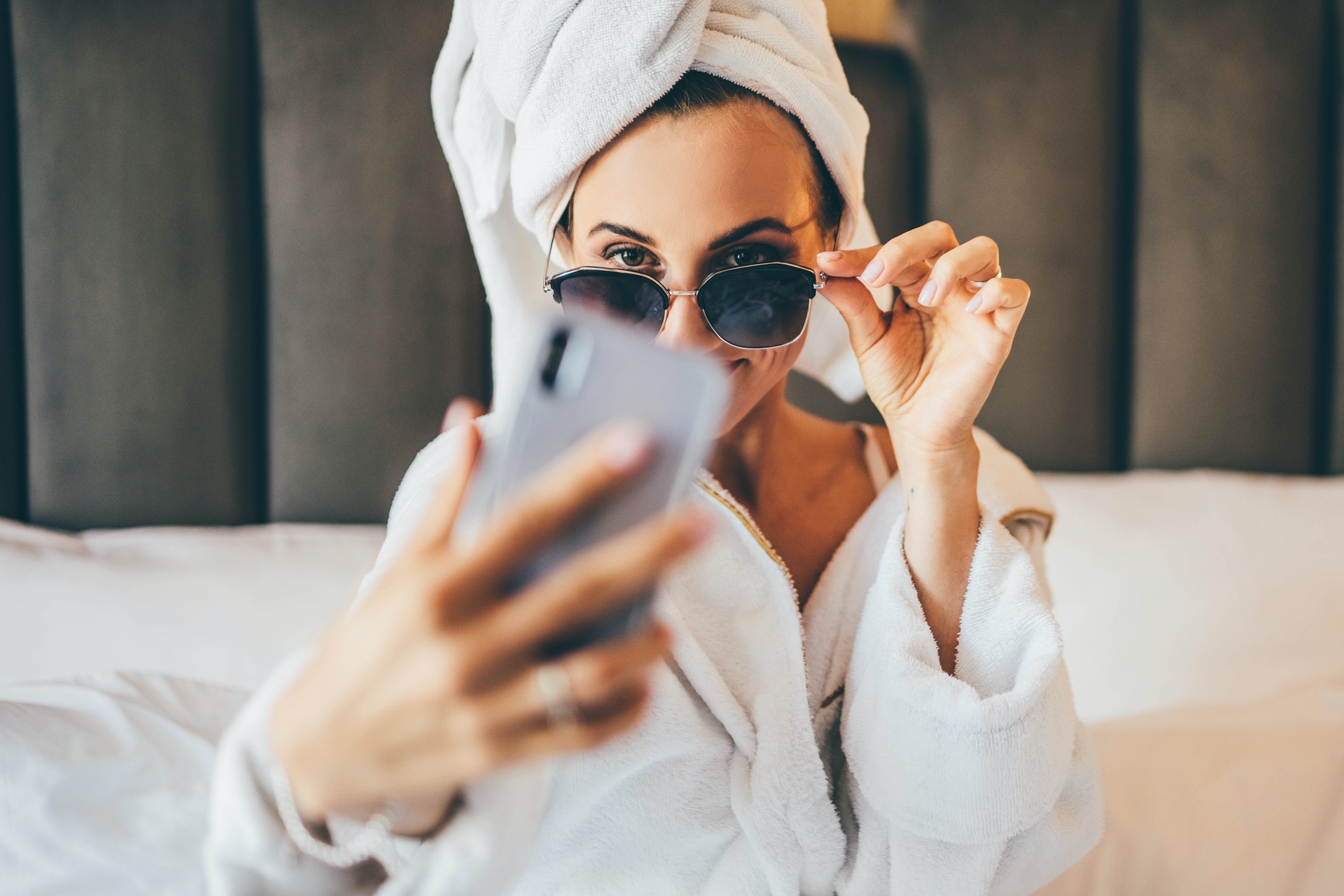 woman in towel and bathrobe sitting, making selfie and having fun