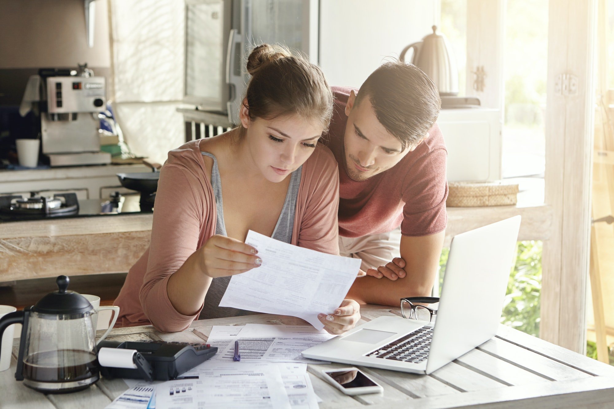 Young couple managing finances, reviewing their bank accounts using laptop computer and calculator a