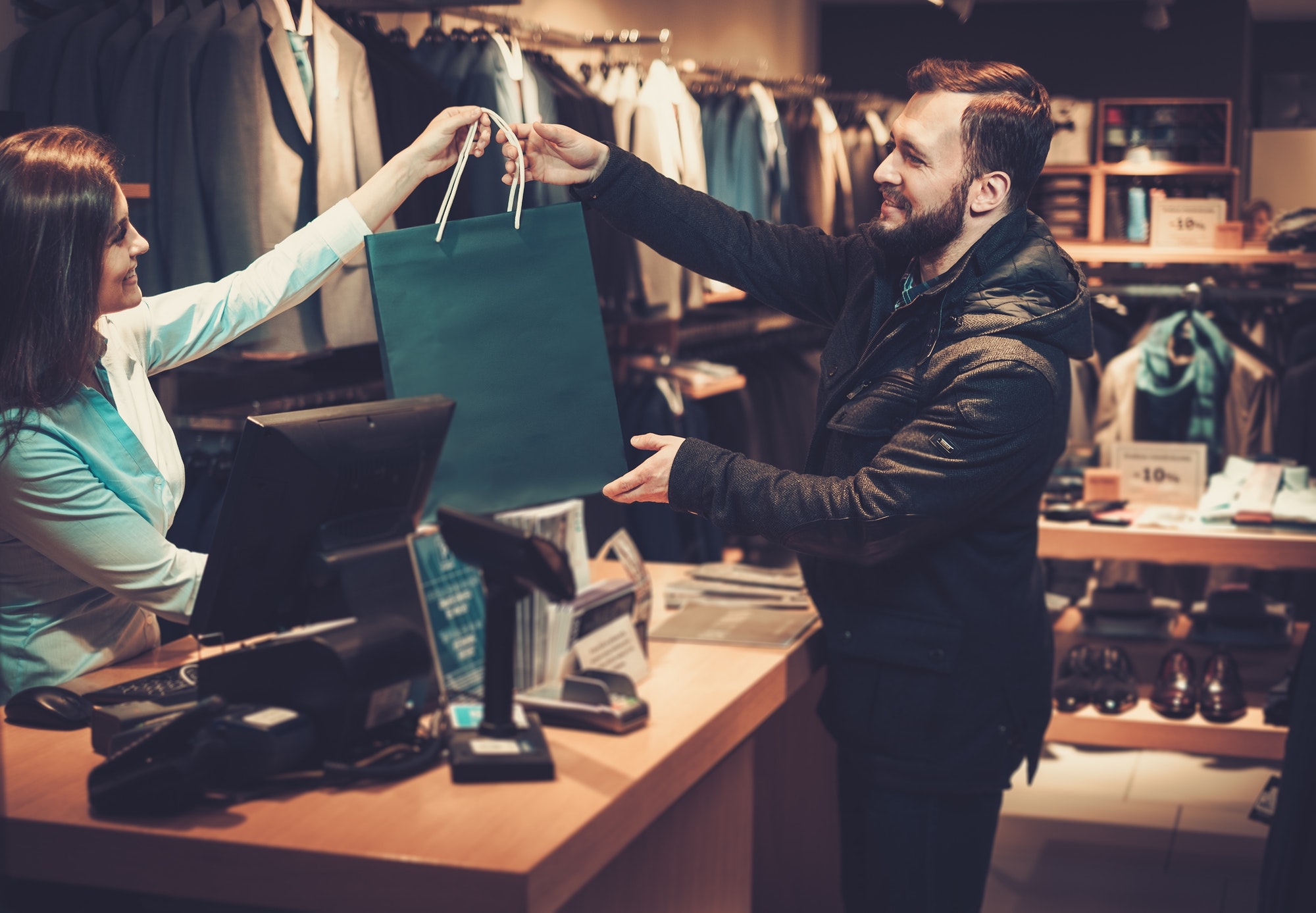 Happy handsome man taking shopping bag from saleswoman in a suit shop.