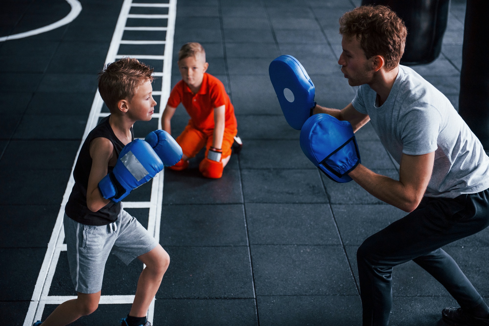 Young trainer teaches kids boxing sport in the gym