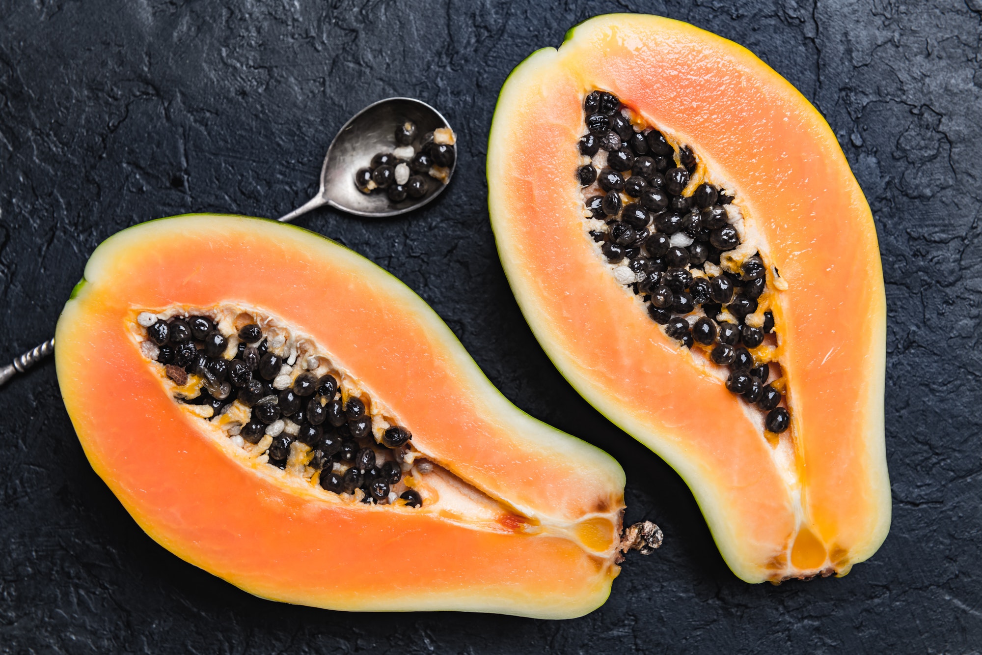 Slised papaya with silver spoon on black concrete background