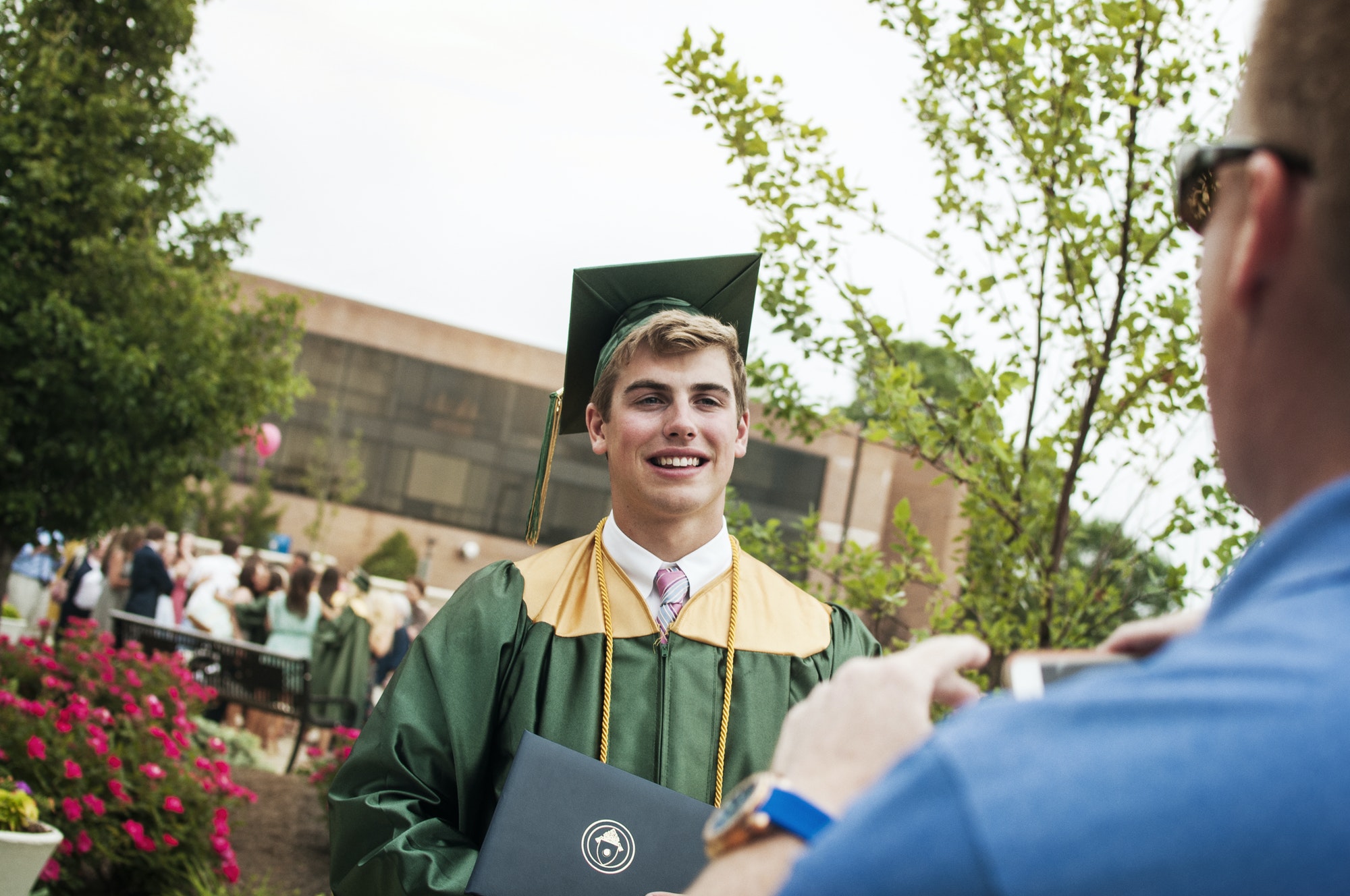 Father Photographing Male Graduate Student In Campus At Graduation Ceremony