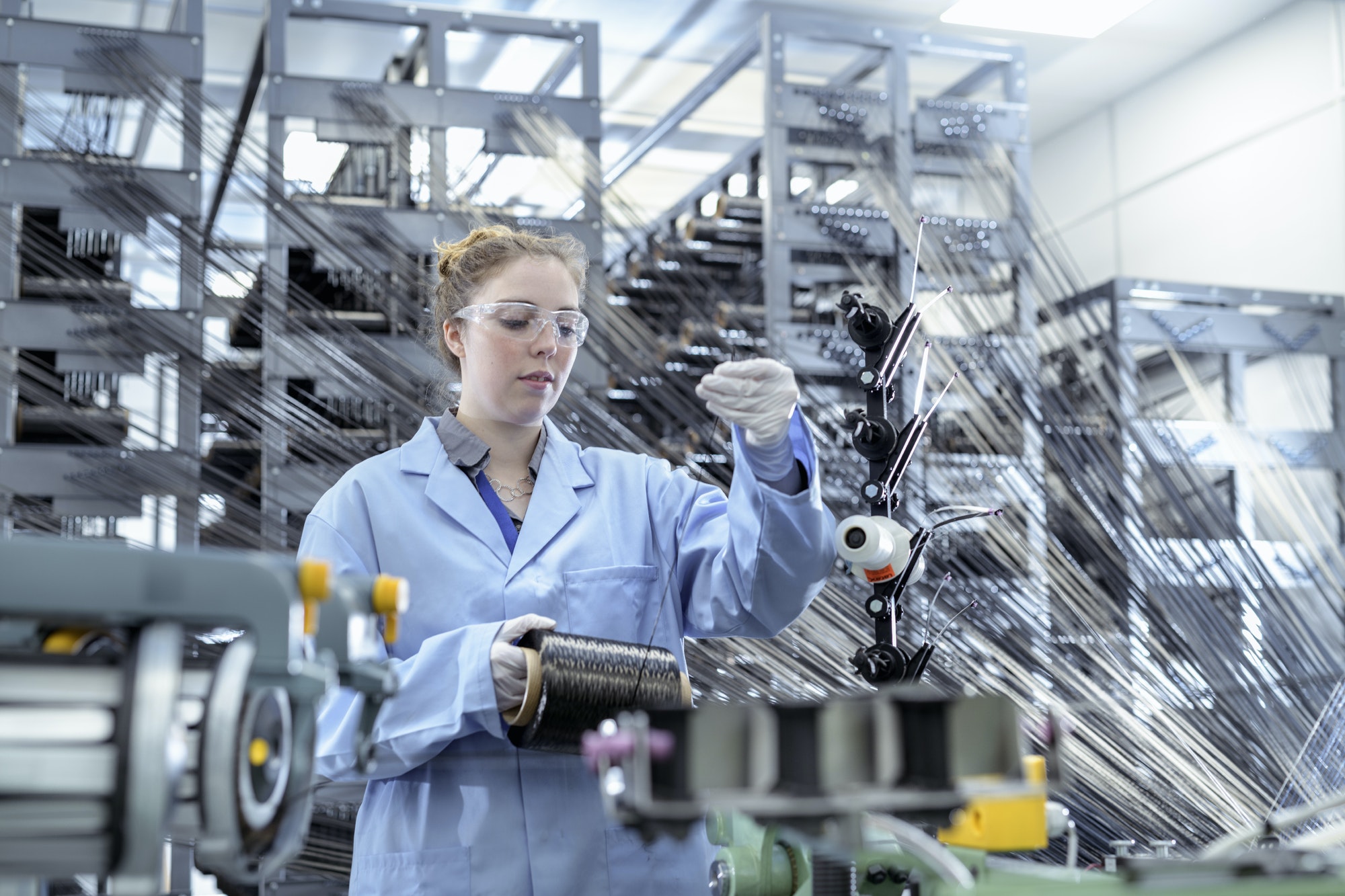 Operator with carbon fibre bobbins on loom in carbon fibre production facility