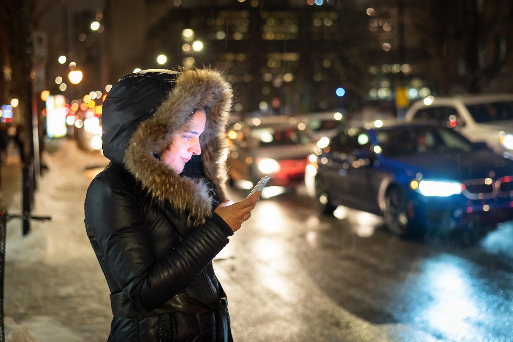 Woman using her phone standing beside a busy street